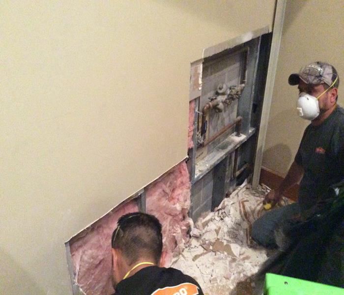 two employees wearing masks and removing drywall and insulation