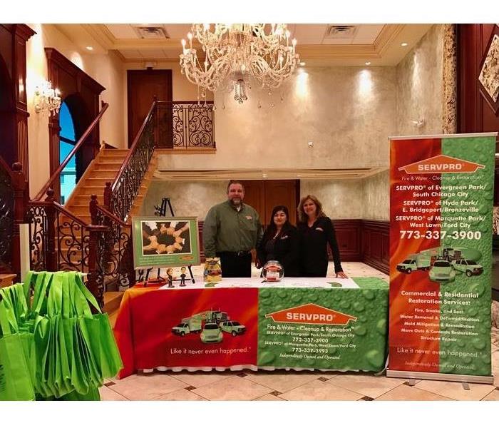 three people standing behind a table with SERVPRO promotional items