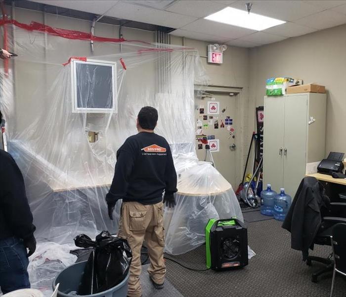 workers taped poly to wall, drying equipment in an office