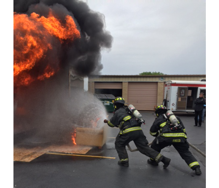 two firefighters spraying a fire from a burn box demonstration