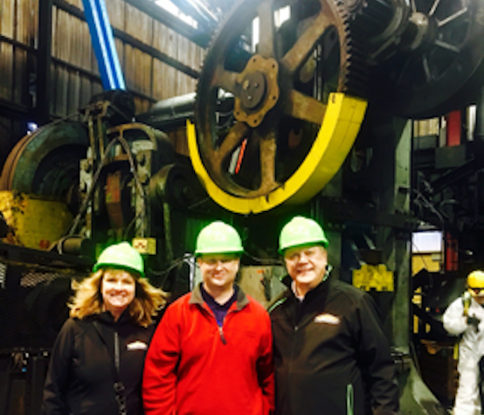 three SERVPRO employees wearing green hardhats in front of a large machine