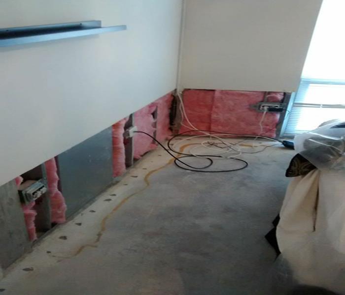 room with exposed concrete floor and the bottom two feet of drywall removed exposing pink insulation