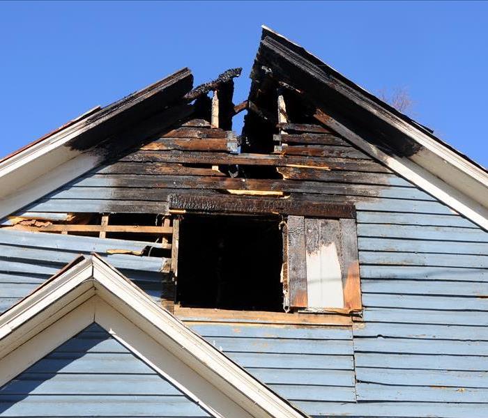 A blue house with part of the roof and window burnt.